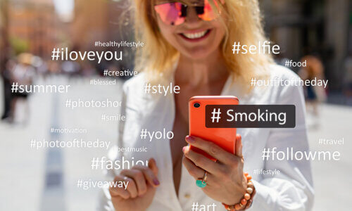 Bild på kvinna som håller en telefon som omgärdas av hashtags, bland annat smoking - för kändisar röker