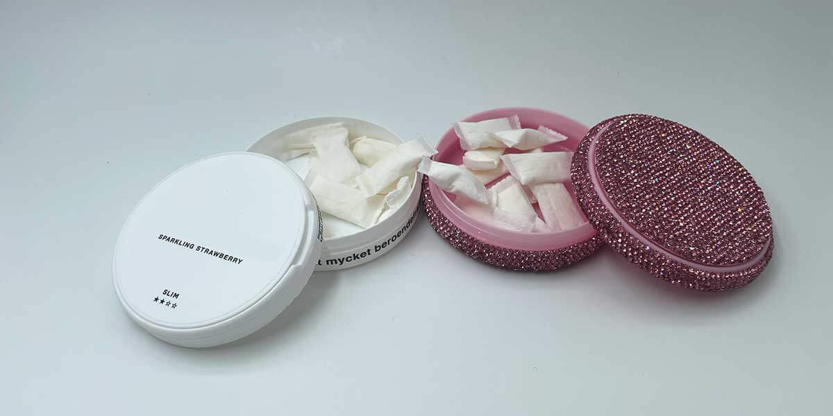 Foto de dos latas de snus, una blanca y otra rosa brillante, que contienen el producto snus blanco.